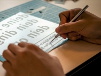 zwei Hände auf einem Tisch, die mit einer Entgitternadel an einem Plotterstück arbeiten