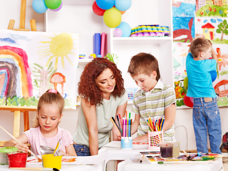 Das Bild zeigt eine Erzieherin und drei Kindern beim Basteln in einem Aufenthaltsraum