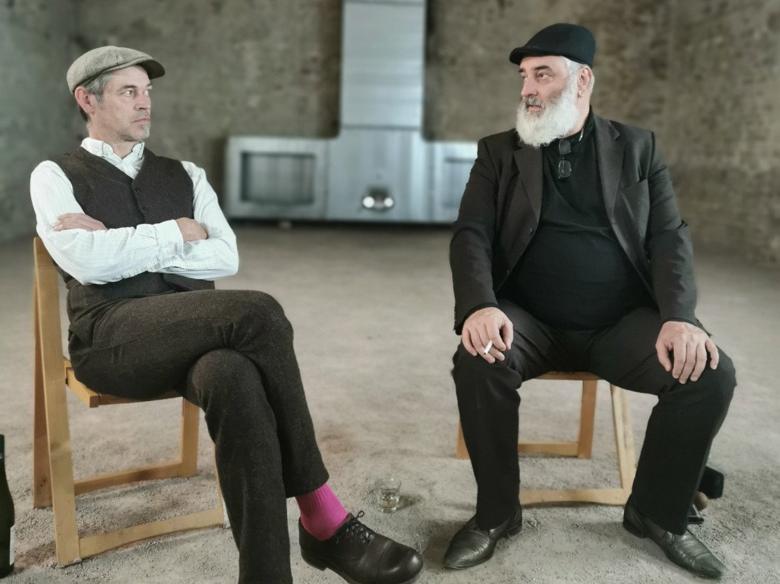 Zwei Männer sitzen auf Stühlen und schauen sich gegenseitig an.