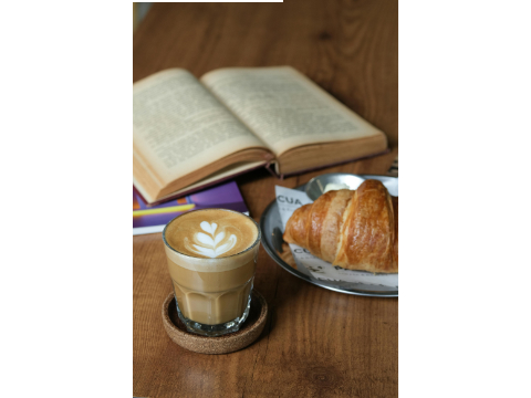 Blick auf einen Tisch mit einem aufgeschlagenen Buch, Milchkaffé und Croissant