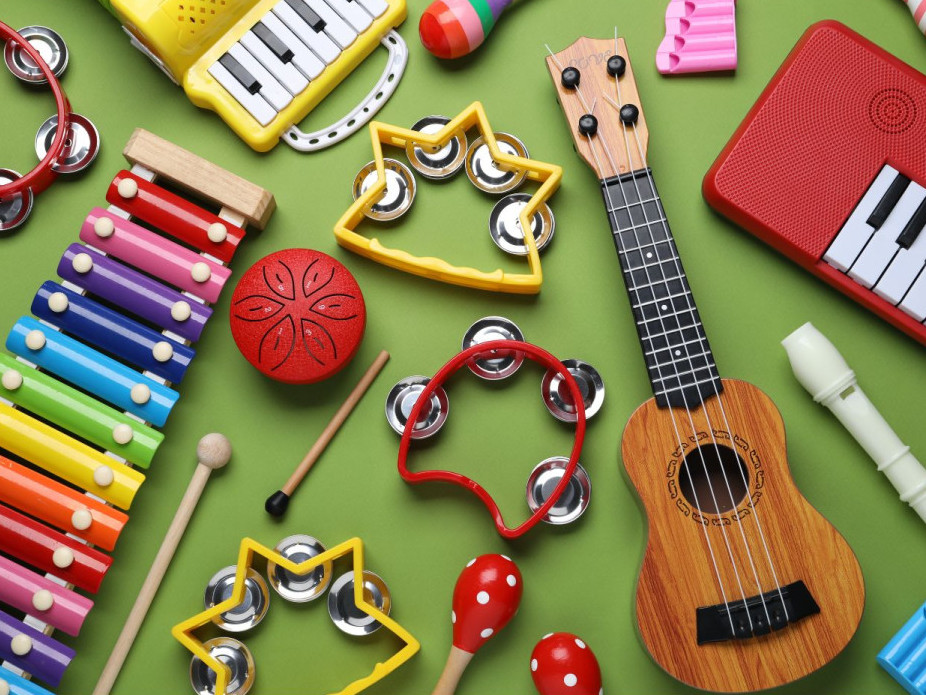 Bunte Auswahl an Kinder-Musikinstrumenten wie Xylophon, Ukulele, Rasseln und Tamburinen auf grünem Hintergrund.