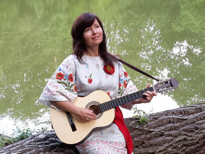 Sängerin Natalia Natalevych sitzt mit ihrer Gitarre auf einem Baumstamm am See