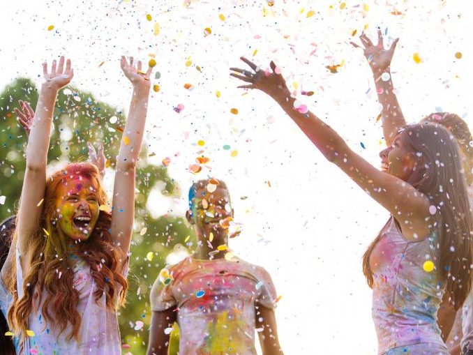 Gruppe junger Menschen wirft buntes Konfetti in die Luft und feiert draußen im Sonnenlicht.
