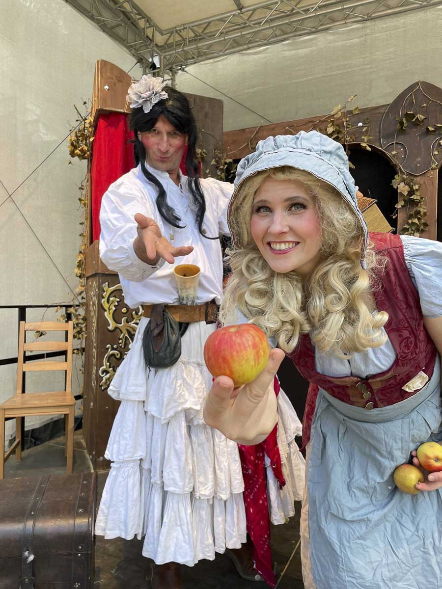 Verkleidete Männer und Frauen. Die Frau hält einen Apfel in der Hand.