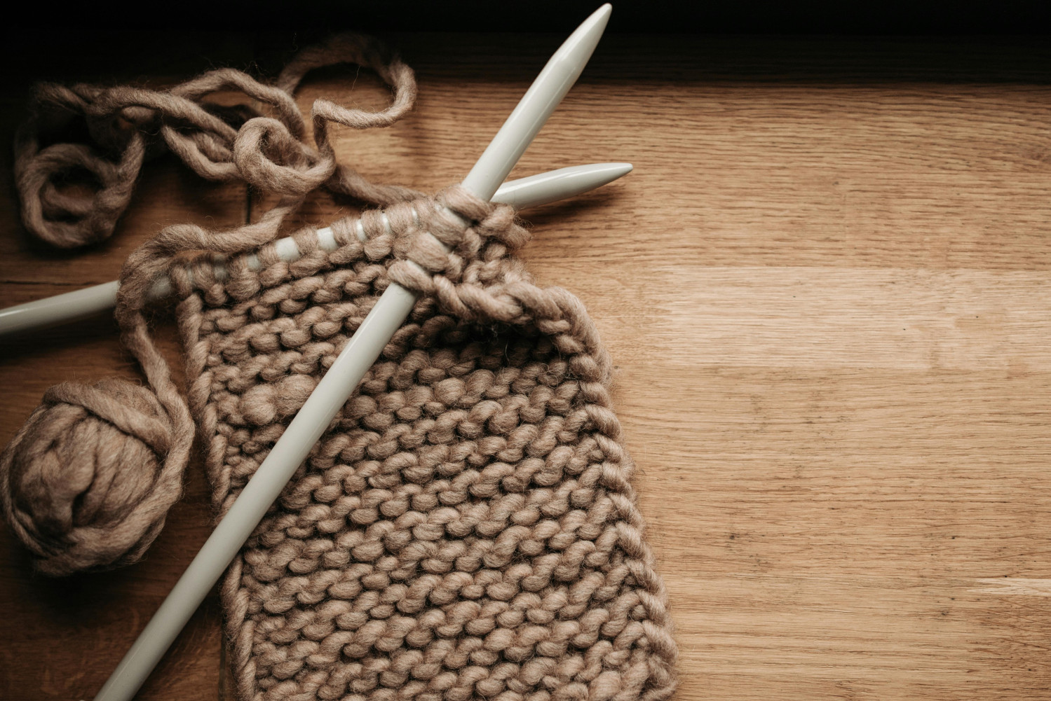 Angefangenes Strickprojekt aus brauner Wolle liegt auf einem Tisch