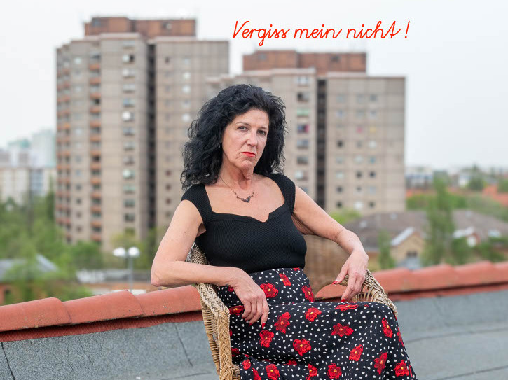 Eine Frau sitz auf dem Stuhl auf einem Dach und im Hintergrund sind zwei hohe Plattenbauhäuser
