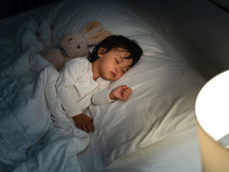 schlafendes Kind mit Plüschhase in Bett