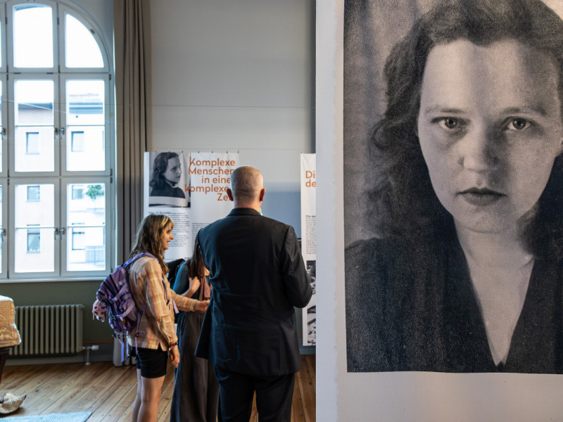 Im Vordergrund ein Panel mit Portraitansicht von der Schriftstellerin Susanne Kerckhoff, im Hintergrund Besuchende der Ausstellung.