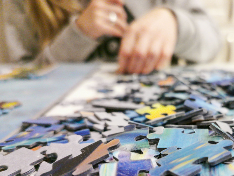Lose Puzzleteile im Vordergrund. Im Hintergrund unscharf eine Person die puzzelt.