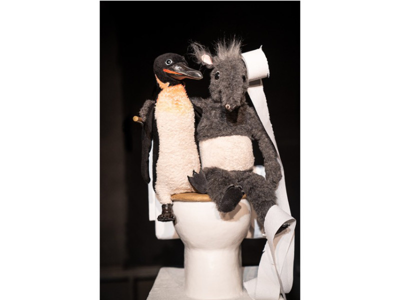 Szenenbild: ein Plüsch-Pinguin und ein Plüsch-Tapir sitzen zusammen auf einer Toilette