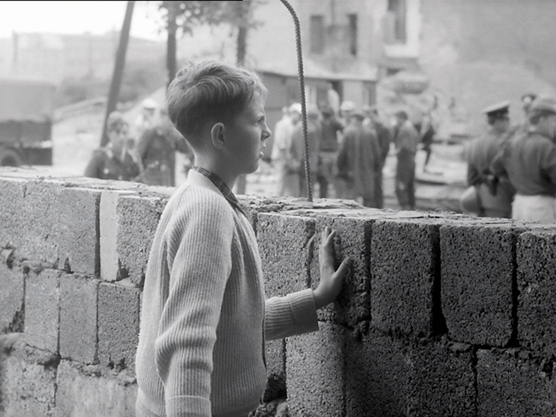 Ein Junge beobachtet den Bau der Mauer und legt die Hand auf die frisch gesetzten Steine