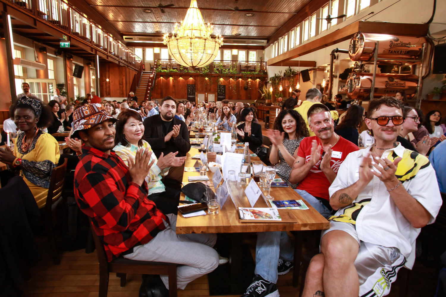 Titelinhaber*innen der Härtefallkommission, Senatorin Cansel Kiziltepe und Staatssekretär Max Landero applaudien auf dem Sommerfest