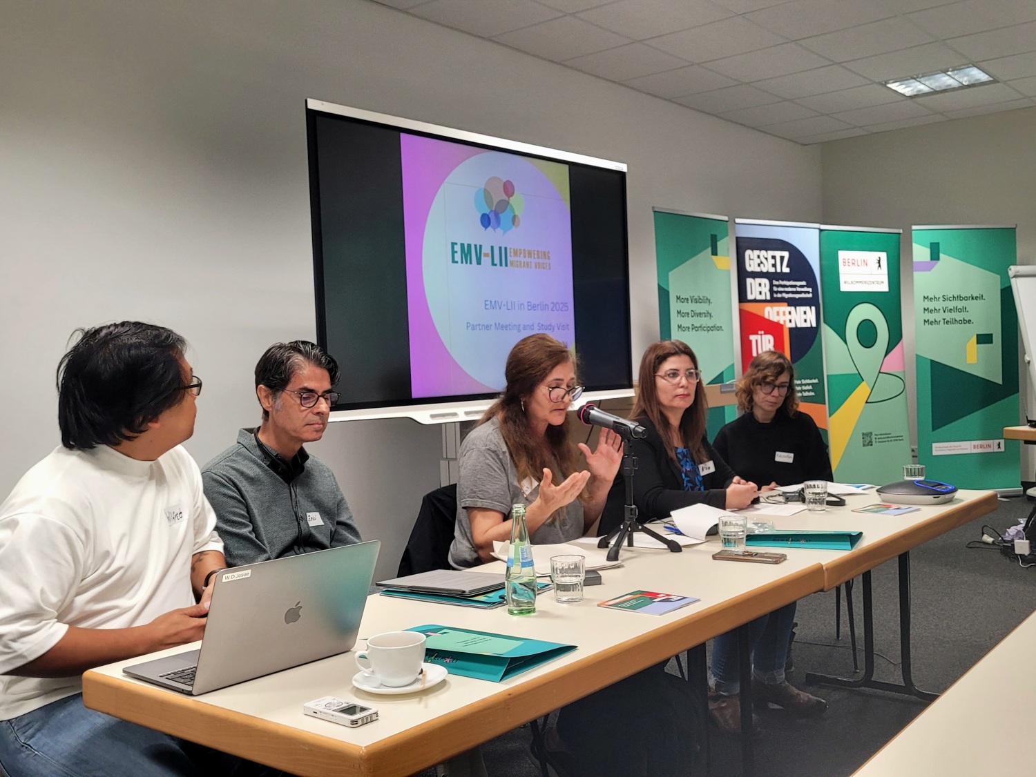 Fünf Personen sitzen an einem Tisch und halten einen Vortrag. Im Hintergrund ist eine Präsentation zu sehen.