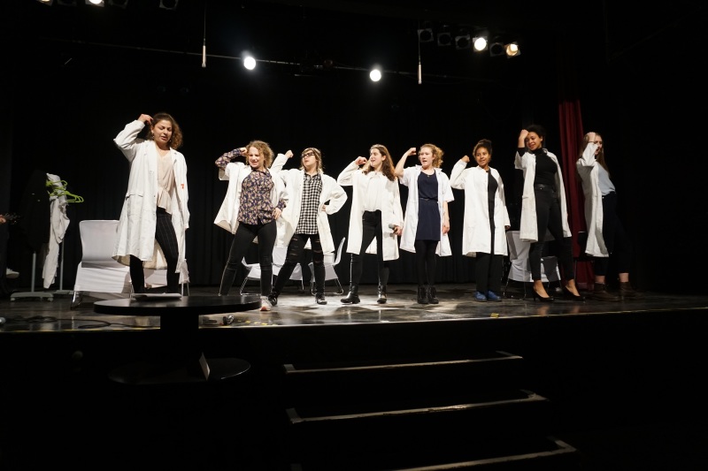 Szene aus dem Musical „Wie fühlst du BUNT“: Eine Gruppe von Wissenschaftlerinnen singt und steht dabei in Siegerpose auf der Bühne