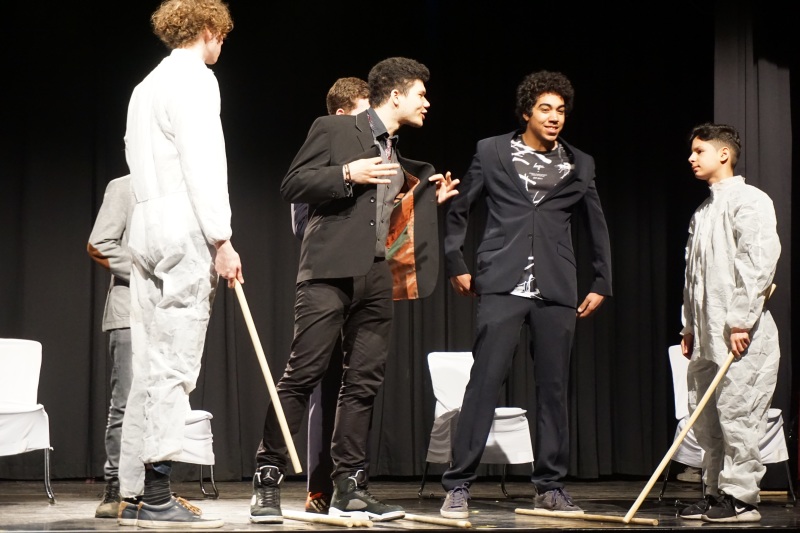 Szene aus dem Musical „Wie fühlst du BUNT“: Maler in Arbeitskleidung werden wegen ihres Aussehens von Männern in Anzügen beleidigt