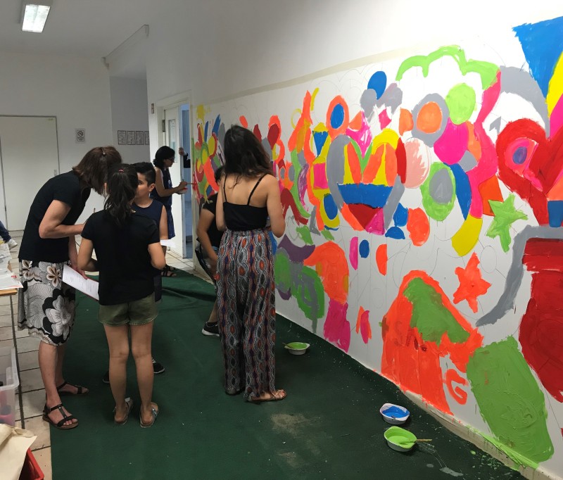 Erwachsene und Kinder bemalen gemeinsam eine Wand im Flur einer Gemeinschaftsunterkunft