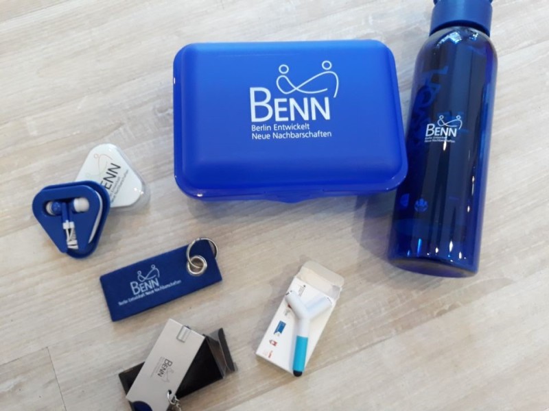 Blaue Brotdose, Trinfflasche, Schlüsselanhänger und Kopfhörer vom Projekt BENN Weißensee (Abkürzung für: "Berlin eröffnet neue Nachbarschaften")