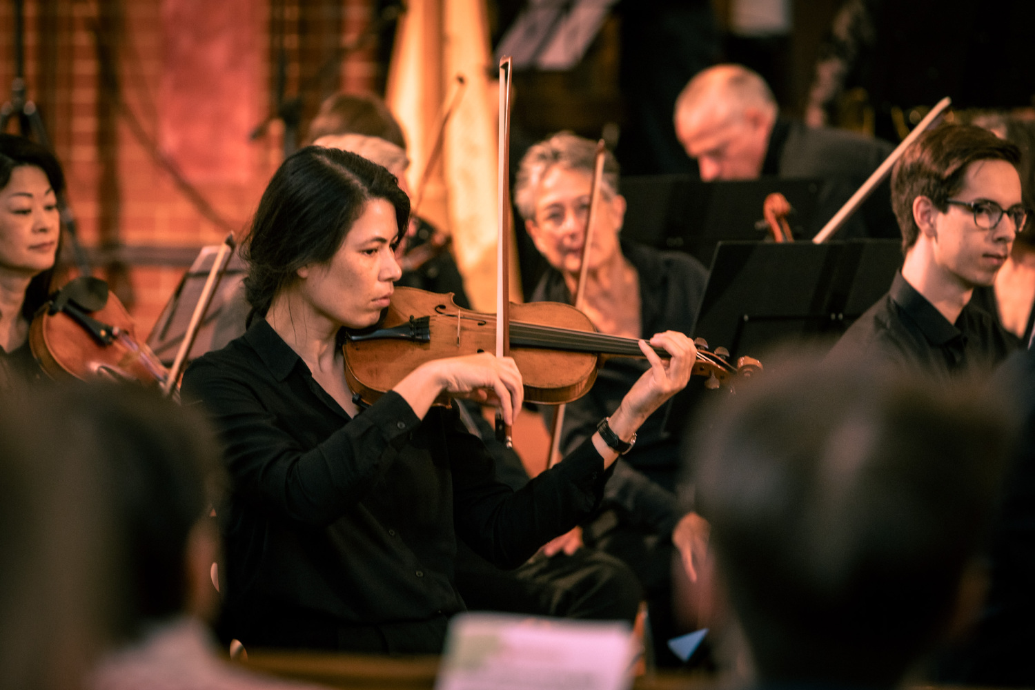 Mehrere Menschen spielen Streichinstruemnte im Orchester