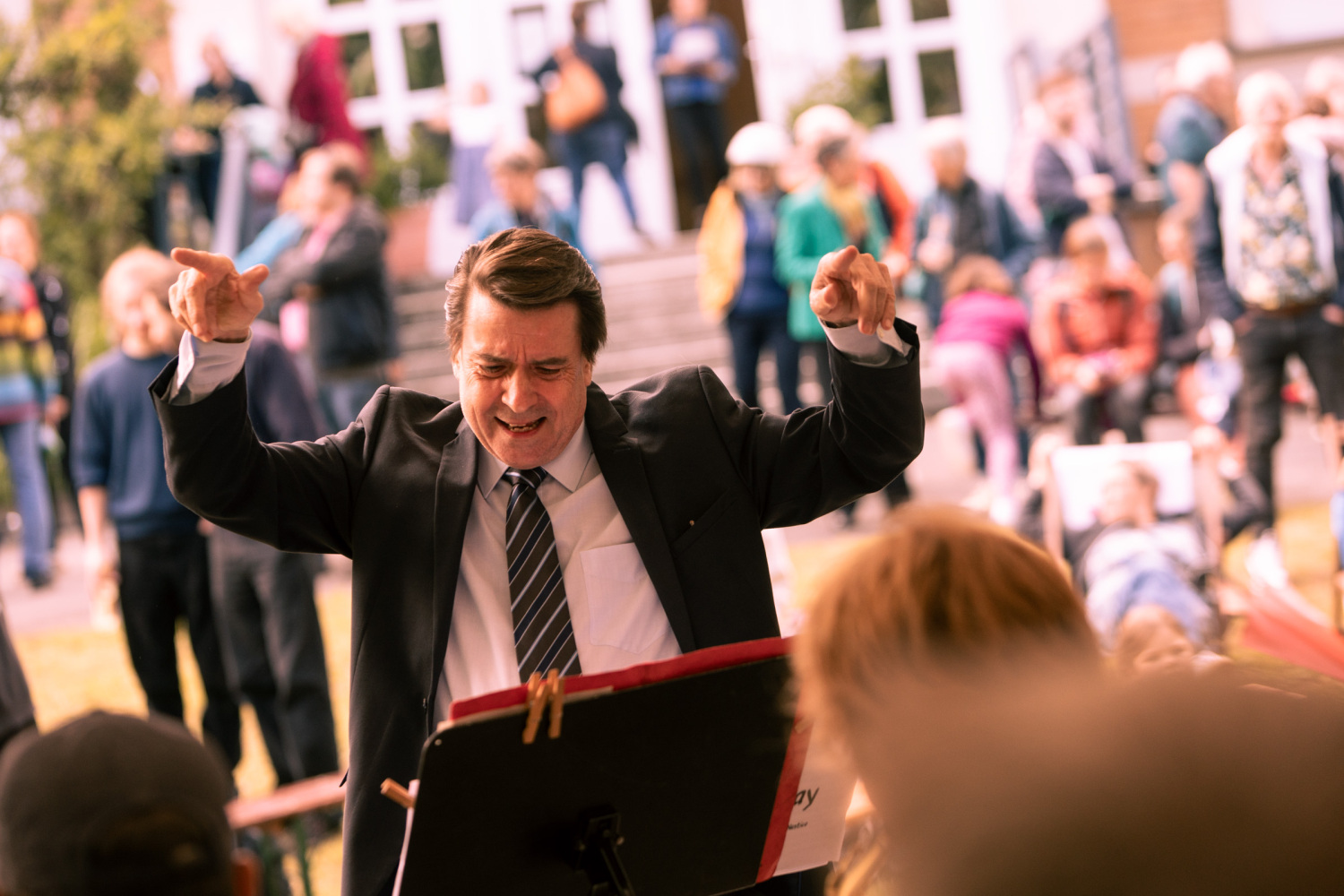 Mann steht vor einem Notanständer und dirigiert eine Jazz Band.