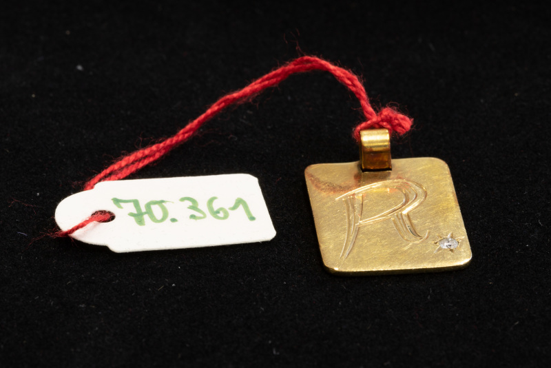 Anhänger, ungestempelt, rechteckige goldfarbene Platte mit Gravur „R“ und einem weißen Stein