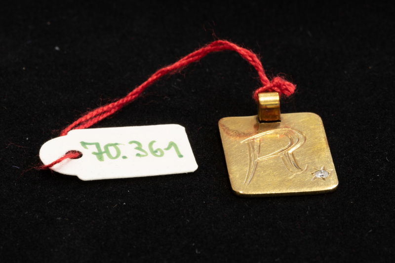 Anhänger, ungestempelt, rechteckige goldfarbene Platte mit Gravur „R“ und einem weißen Stein