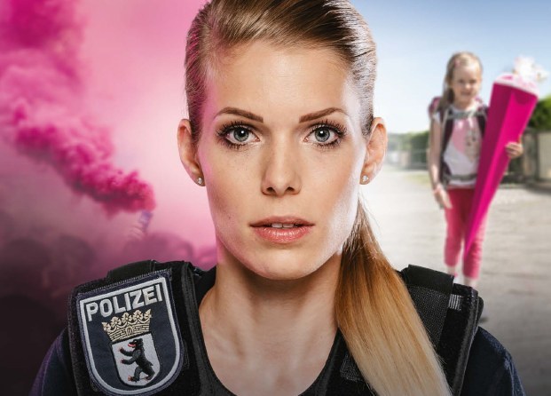 Polizistin im Vordergrund dahinter auf der linken Seite Darstellung einer Demo mit roter Rauchfahne, auf der rechte Seite ein kleines Mädchen mit einer Schultüte