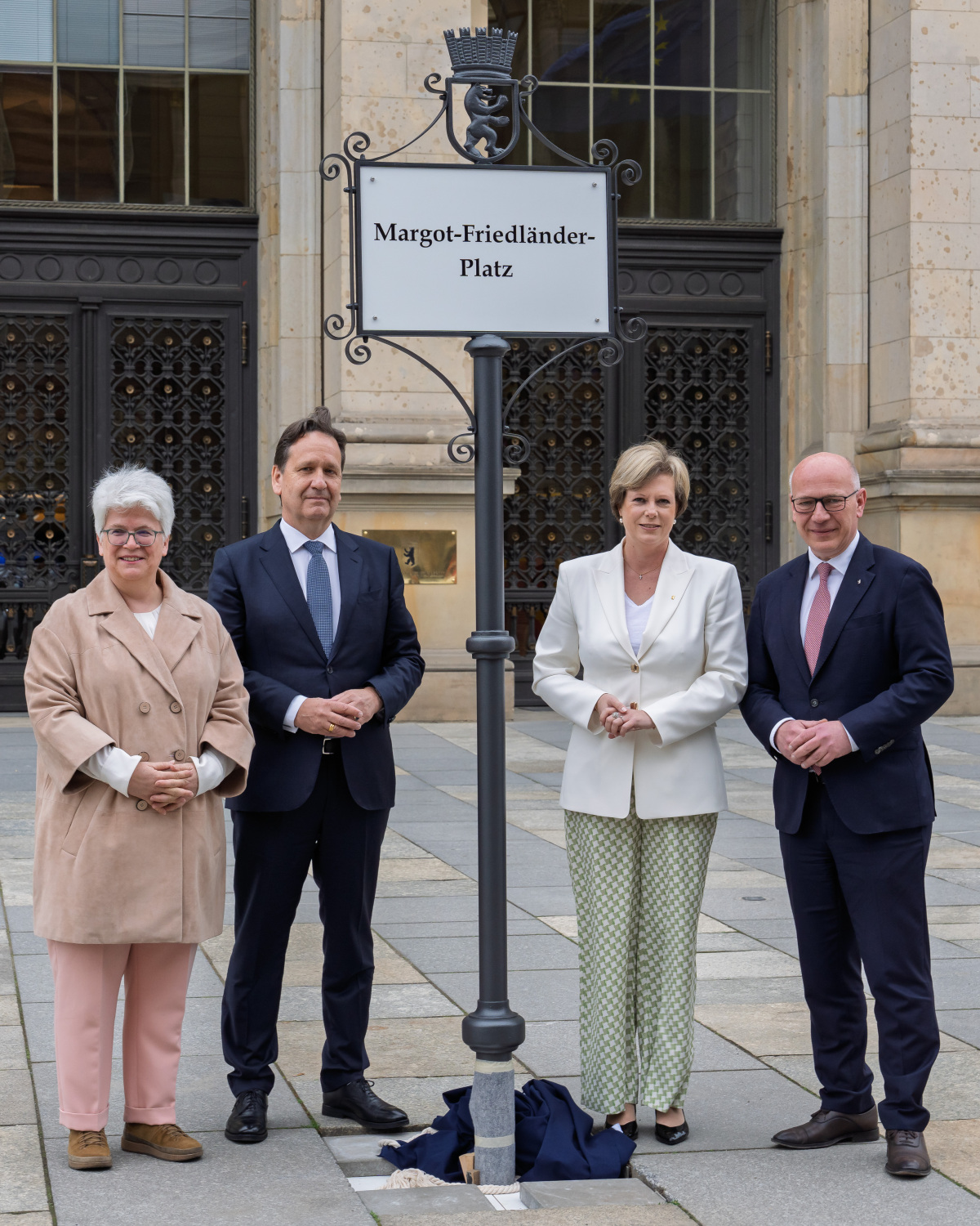 Frau Remlinger, Herr Dreinhöfer, Frau Seibeld und Herr Wegner stehen um das Schild mit der Aufschrift "Margot-Friedländer-Platz"