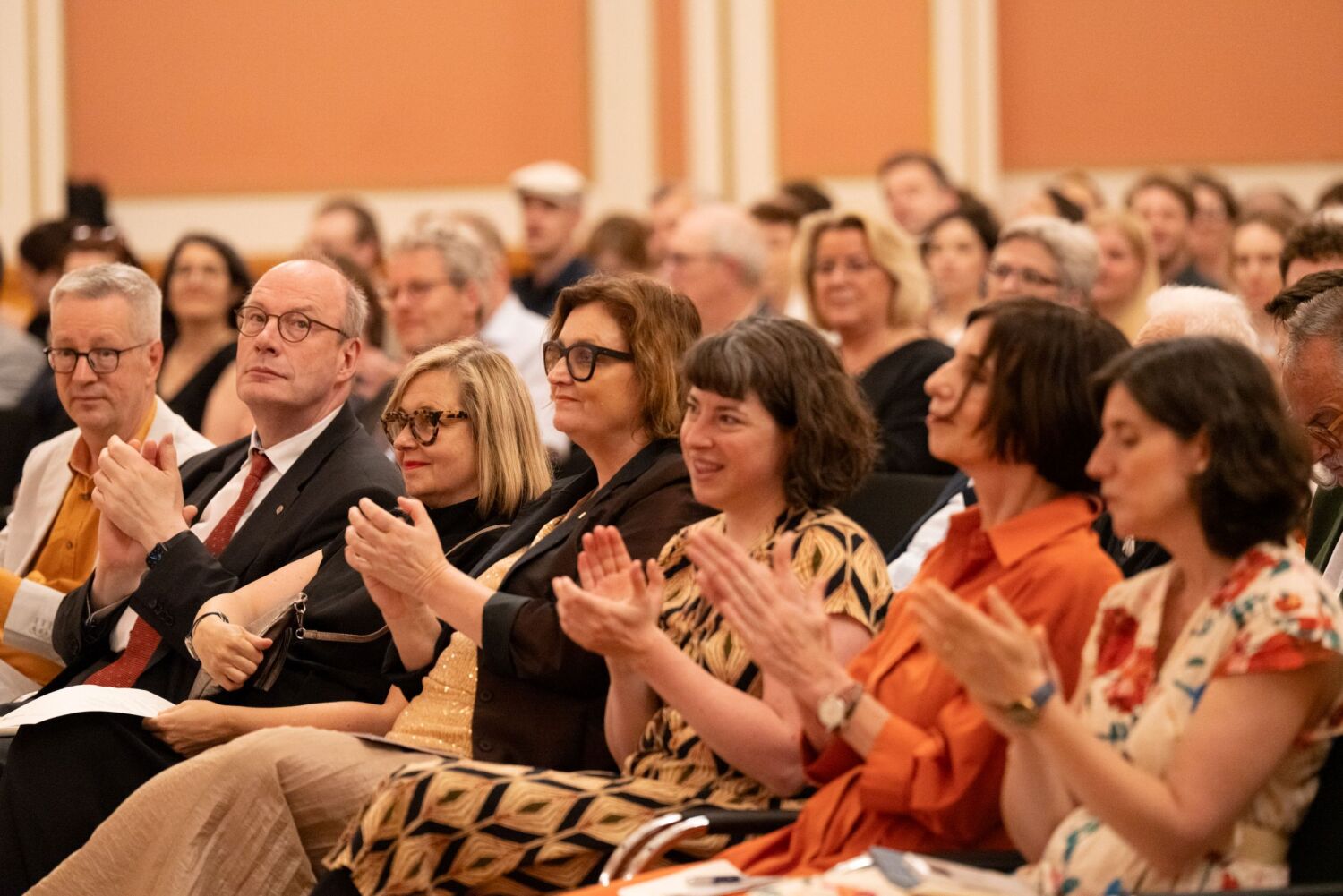 Anita Traninger, Ina Czyborra und Caterina Schürch sitzen in der ersten Reihe des Publikums beim Berliner Wissenschaftspreis und applaudieren.