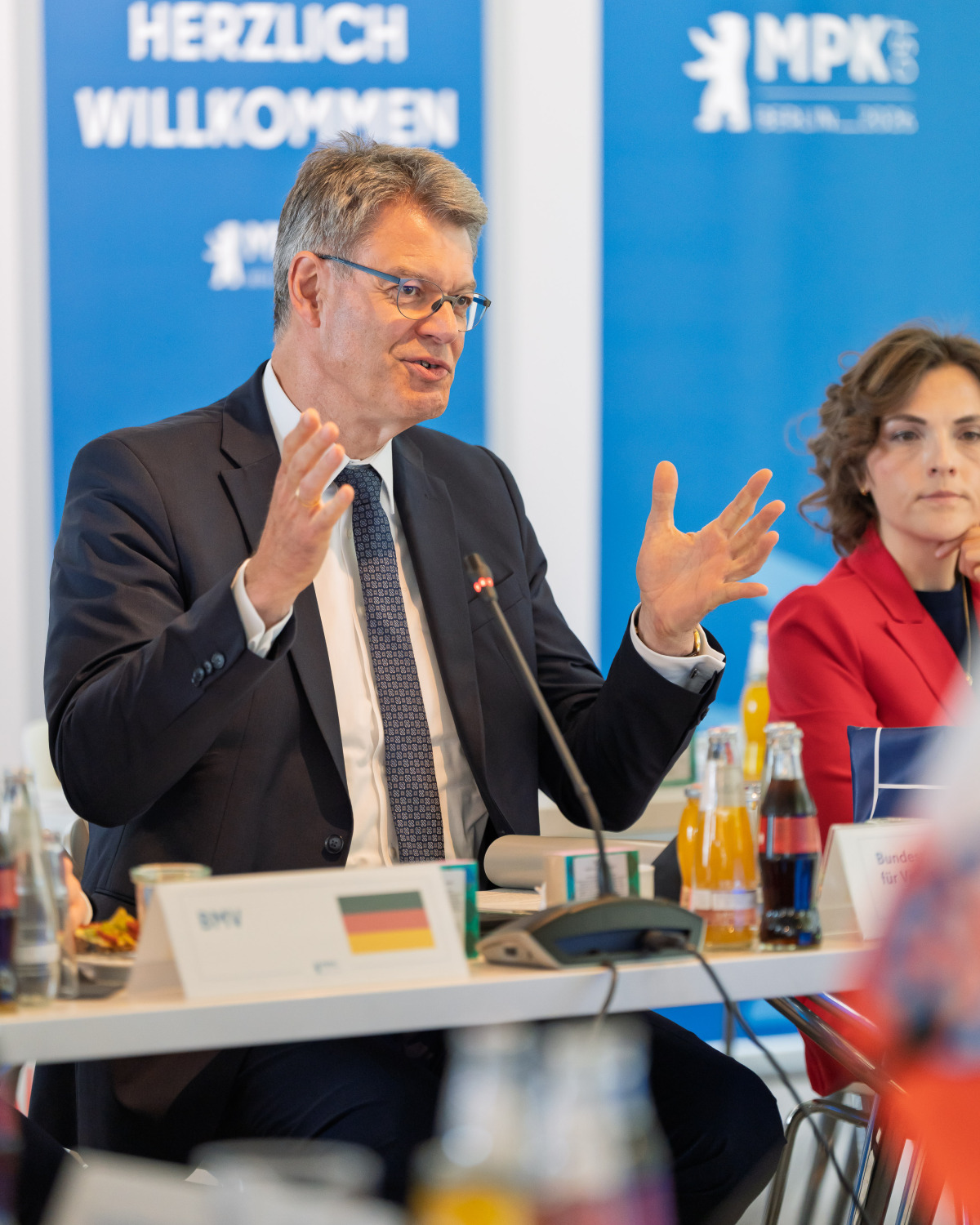 Patrick Schnieder und Elisabeth Kaiser sitzen nebeneinander am Konferenztisch. Patrick Schnieder spricht und macht eine Geste mit den Händen.