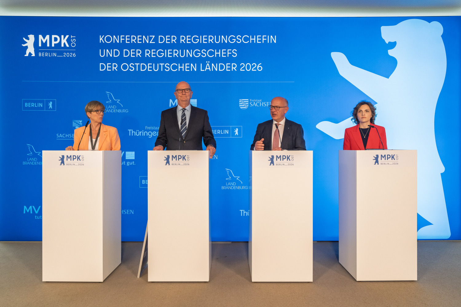 An Redepulten vor einem blauen Banner stehen Christine Richter, Dietmar Woidke, Kai Wegner und Elisabeth Kaiser