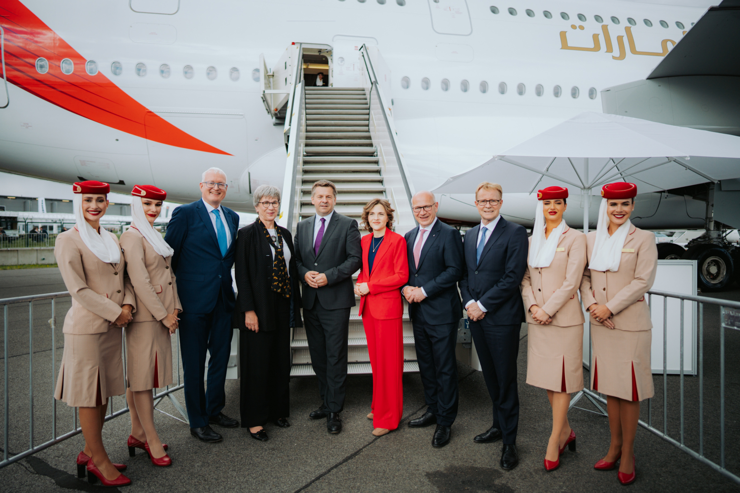 Mario Voigt, Elisabeth Kaiser, Kai Wegner und weitere Personen stehen neben Flugbegleiterinnen in Uniform vor einem Flugzeug der Airline Emirates