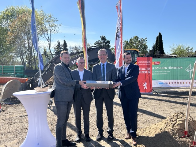 4 Personen auf einer Baustelle, die einen Grundstein gemeinsam halten