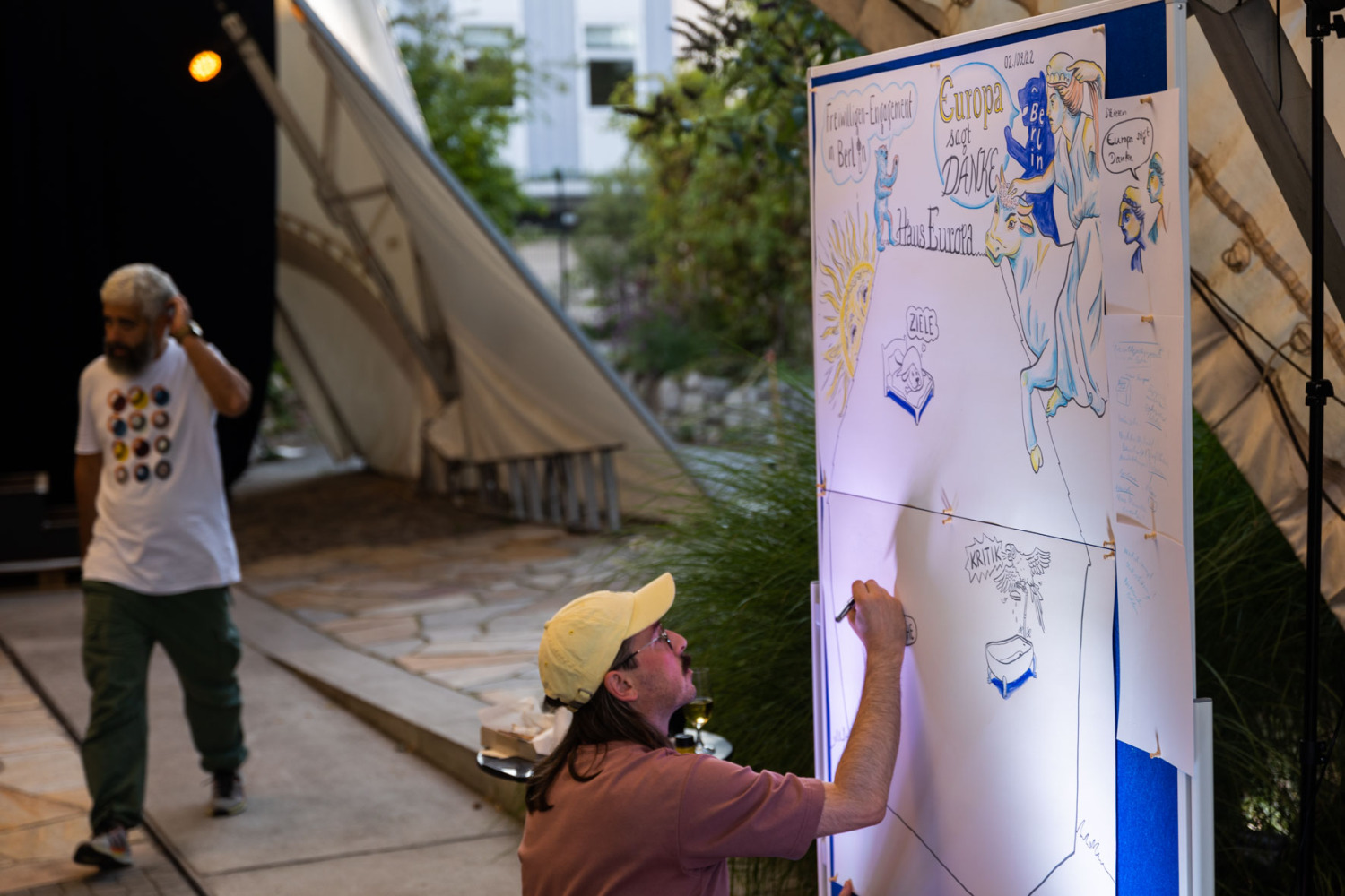 Mann mit Käppi malt großes Bild auf einer Leinwand