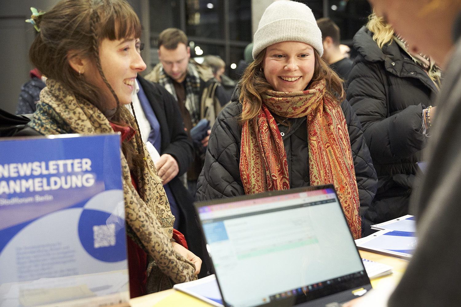 Zwei Frauen in stehen vor einem Anmeldecounter. Im Vordergrund ist ein Laptop.