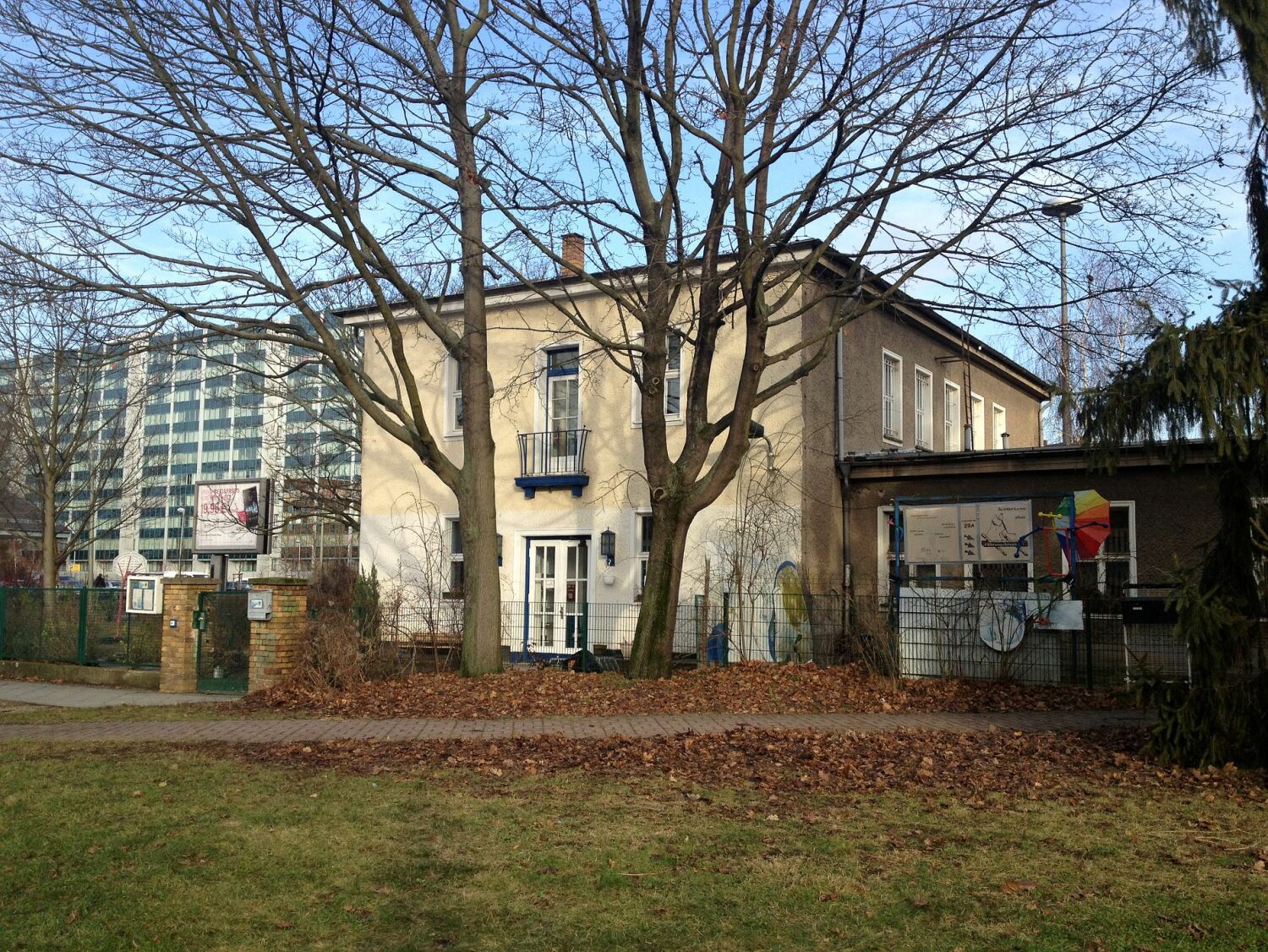 Älteres, zweistöckiges Gebäude mit flachem Anbau, im Hintergrund Plattenbau