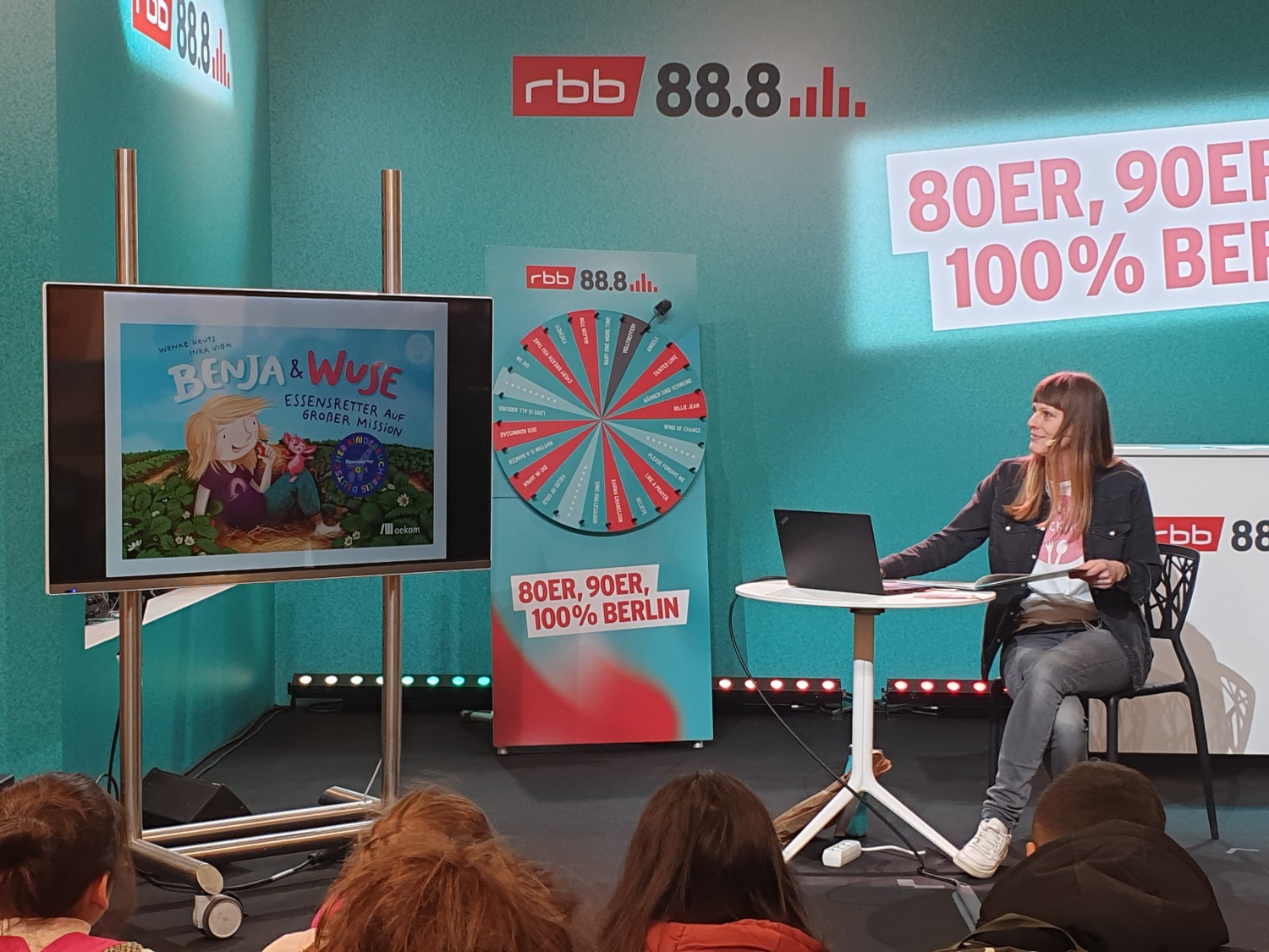 Wenke Heuts präsentiert auf einem Monitor das Buch Benja und Wuse auf der rbb Bühne