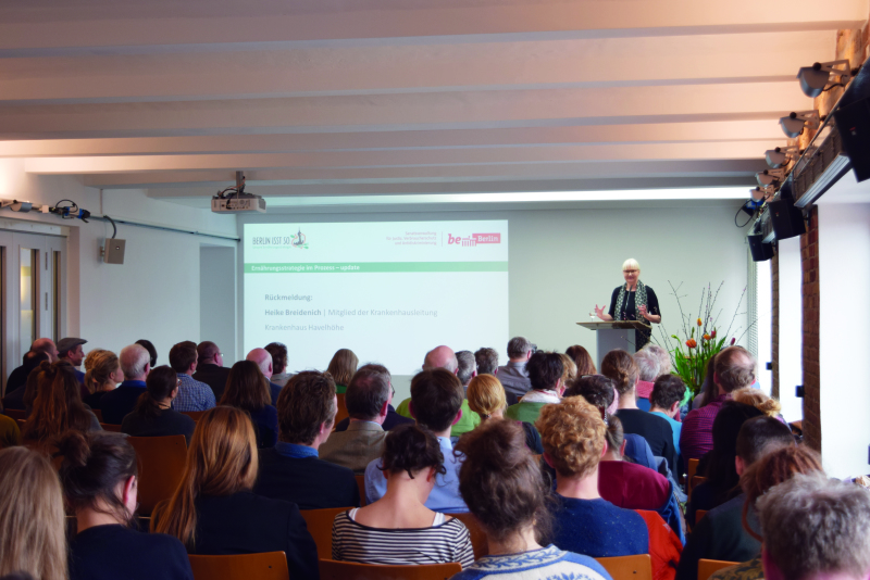 Heike Breidenich, Mitglied Krankenhausleitung Havelhöhe an einem Pult vor Publikum bei einer Leinwand-Präsentation