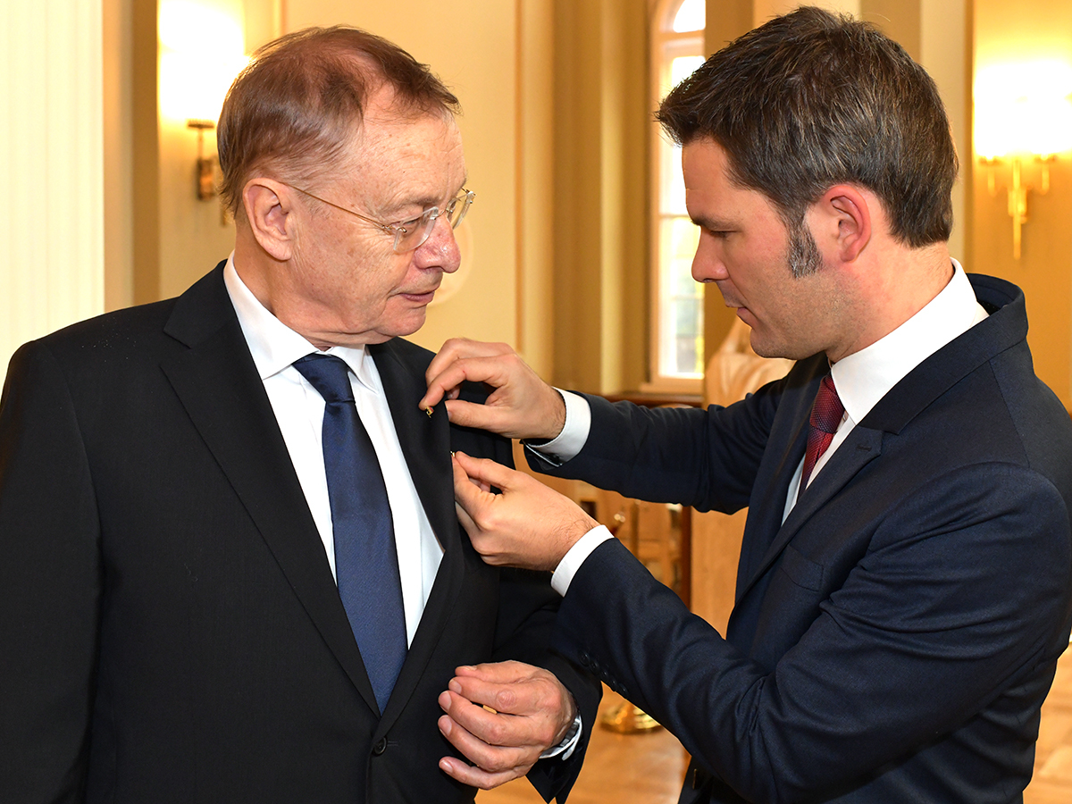 Staatssekretär Steffen Krach steckt Prof. Hajo Funke das Bundesverdienstkreuz an