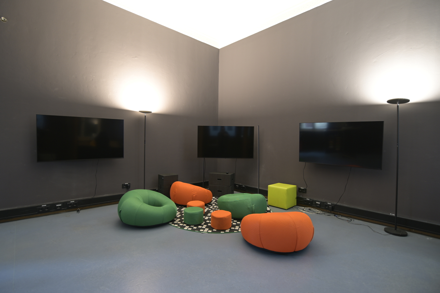 GameMaker Lounge in der Bibliothek am Luisenbad, mit drei Monitoren an der Wand, davor mehrere bunte Sitzkissen