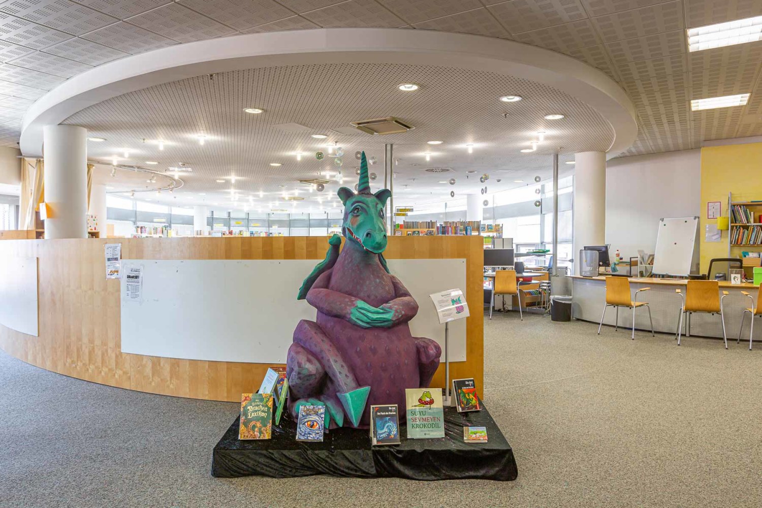 türkis-lila Drachen in der Kinderbibliothek sitzend