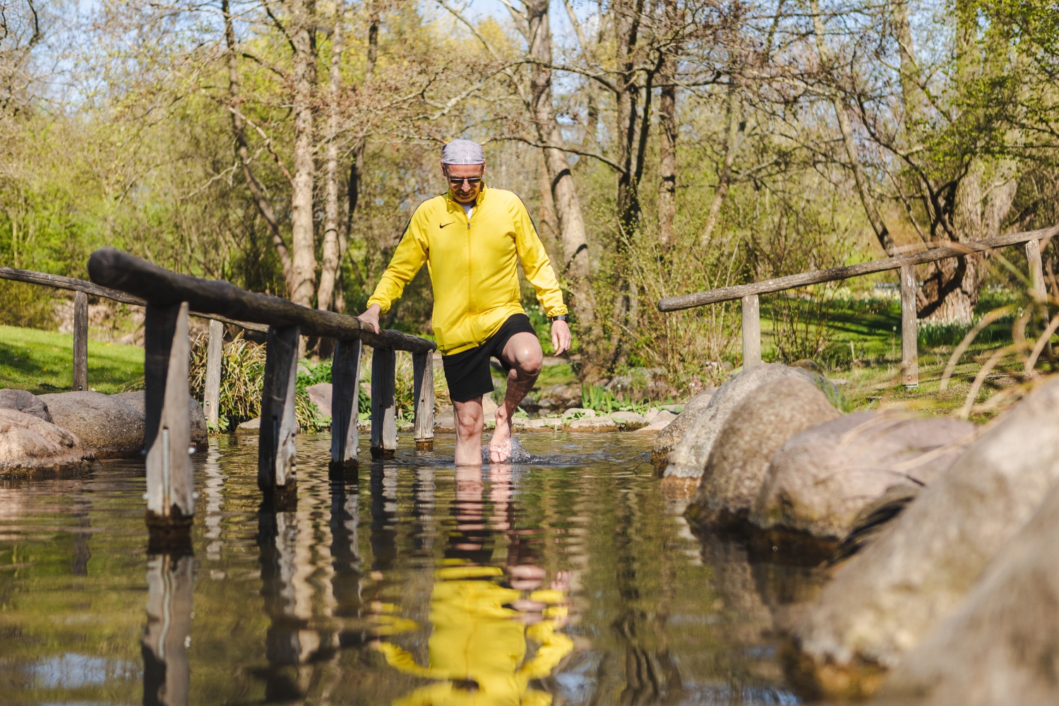 Ein Mann in einer gelben Jacke und hochgekrempelten Hosenbeinen. Er watet gerade durch Wasser 