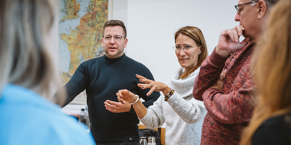 Teilnehmende diskutieren und gestikulieren stehend im Raum